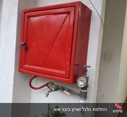 ארון כיבוי אש אדום מותקן על קיר עם צנרת וחיבורי מים
